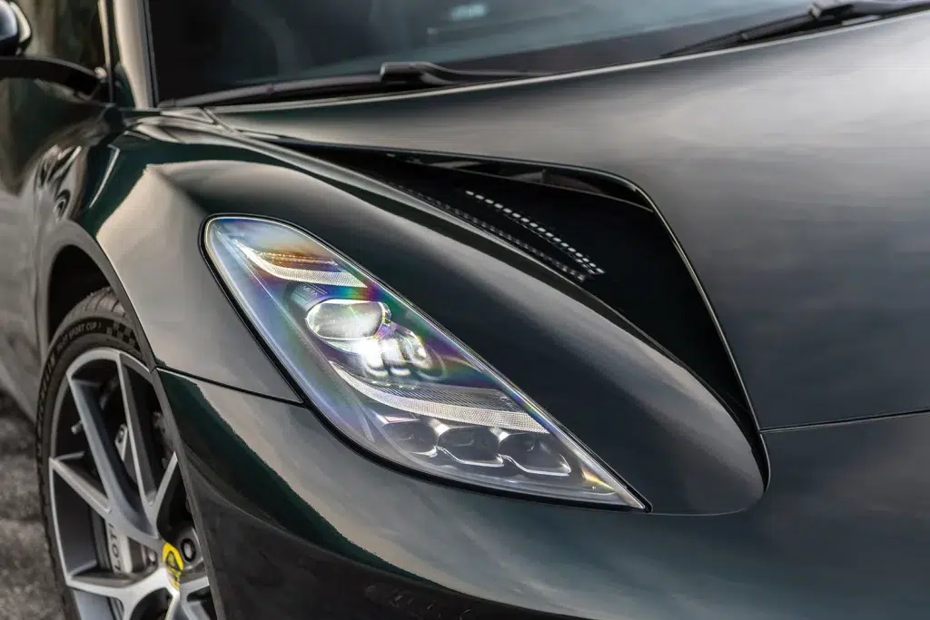 Dunkelgrüner Lotus Emira: Vordere linke Seite mit leuchtendem Scheinwerfer.