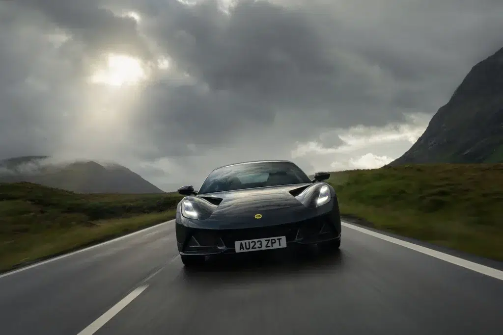 Dunkelgrauer Lotus Emira auf nasser Bergstraße unter dramatischem Wolkenhimmel