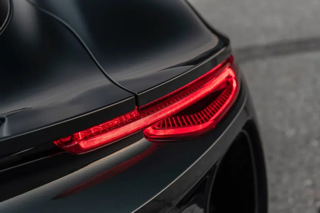 Nahaufnahme der eleganten, leuchtenden roten Rückleuchten eines dunklen Sportwagens.