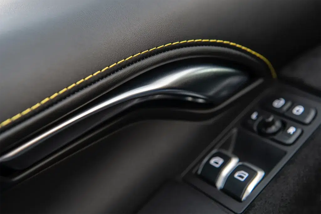 Nahaufnahme der schwarzen Türverkleidung im Innenraum eines Lotus Emira mit gelben Ziernähten, Türgriff und Fensterhebern.