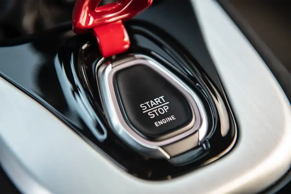 Lotus Emira Innenraum: Nahaufnahme des Start-Stopp-Knopfes mit rotem Zierelement.