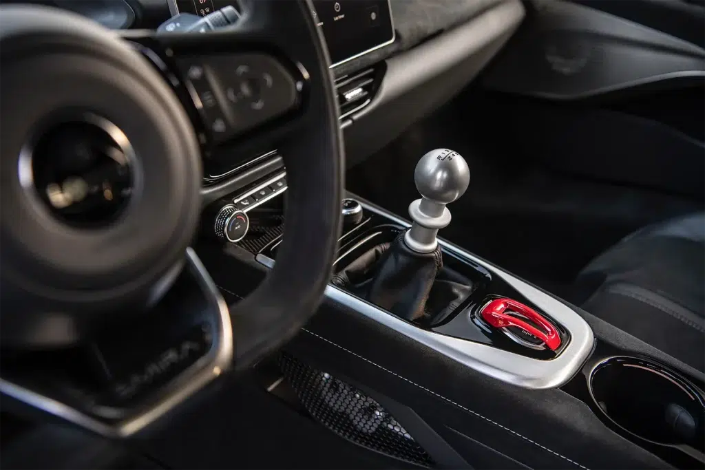 Innenraum des Lotus Emira mit silbernem manuellem Schaltknauf, Lenkrad und rotem Startknopf.