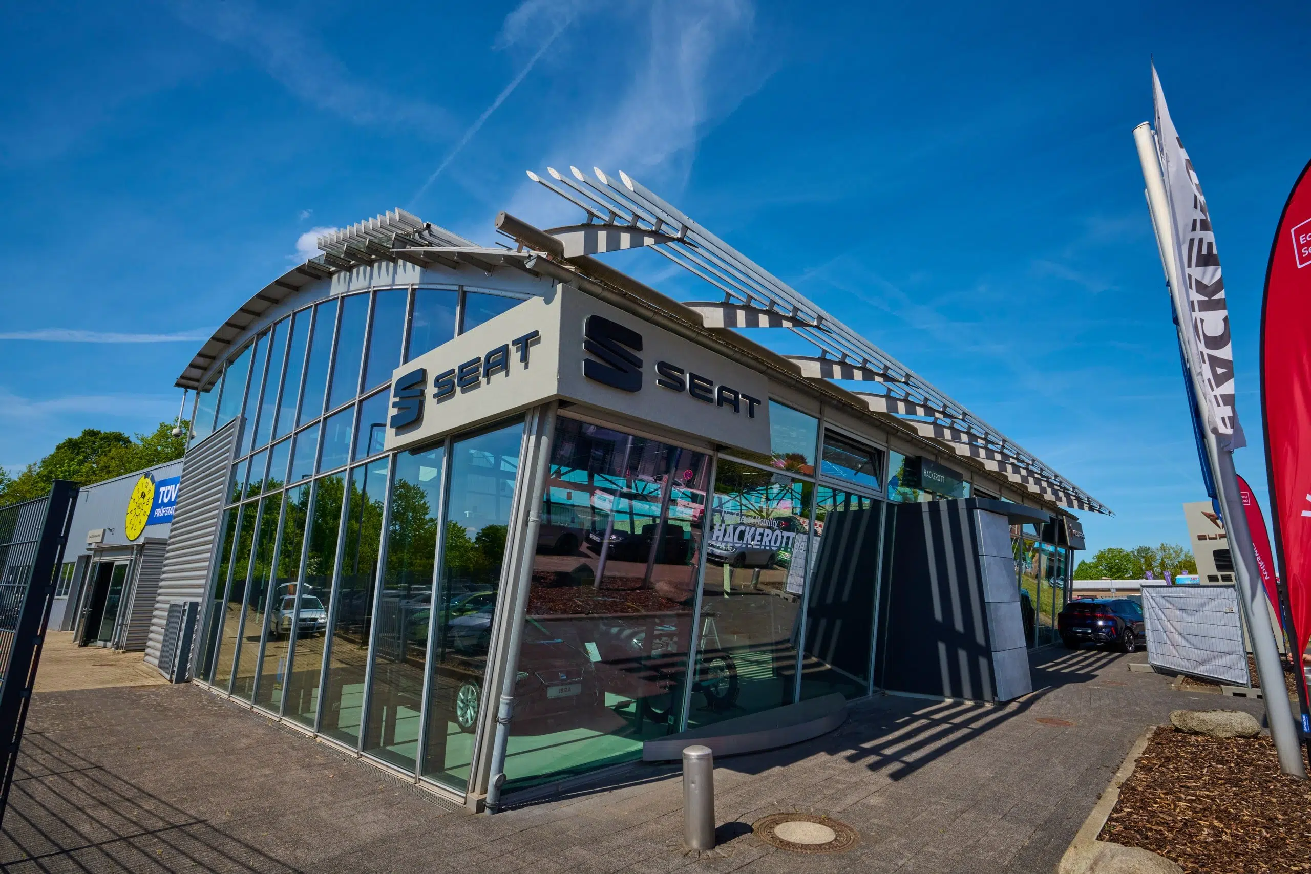Modernes Seat Autohaus Hackerott mit Glasfassade und angrenzender TÜV Prüfstation.
