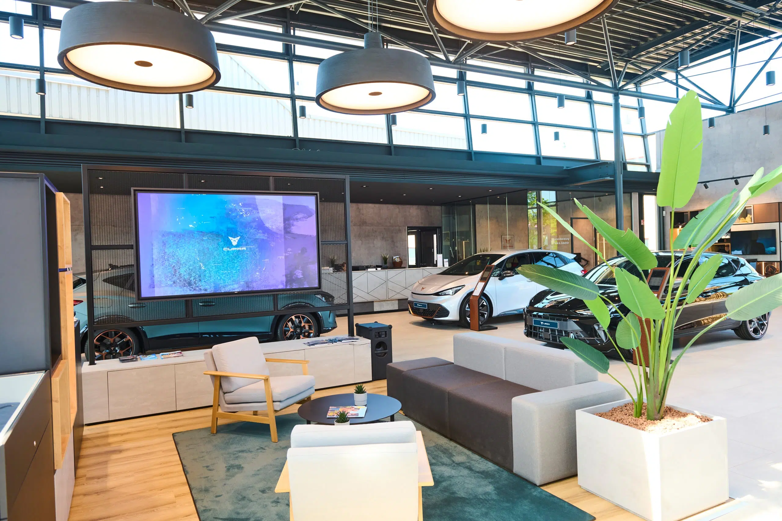 Moderner Cupra Showroom mit ausgestellten Fahrzeugen, großem Bildschirm und Lounge-Bereich.