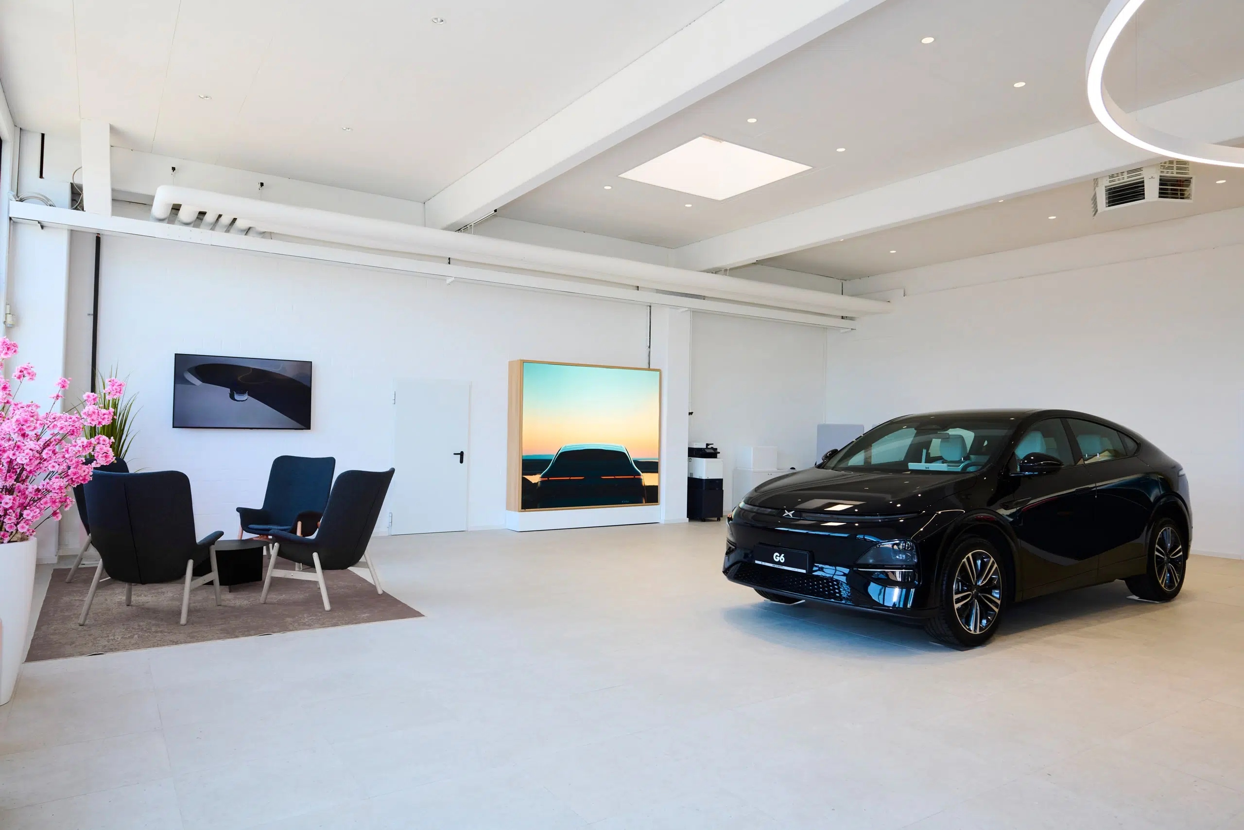 Schwarzer Xpeng G6 in einem hellen, modernen Showroom mit Sitzbereich und Wandbildern.
