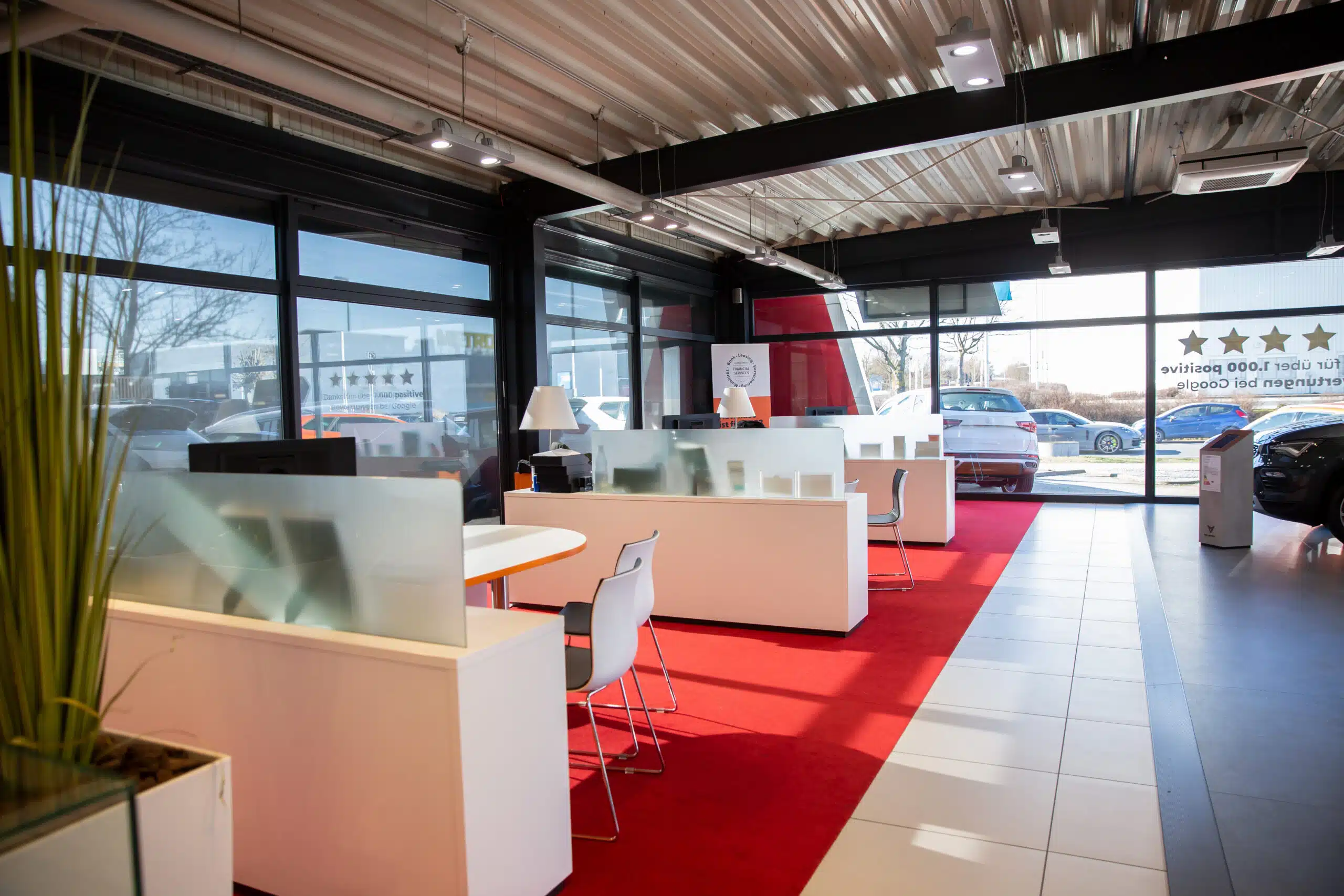 Moderner Showroom eines Autohauses mit Beratungsplätzen, rotem Teppich und Ausstellungsfahrzeugen.