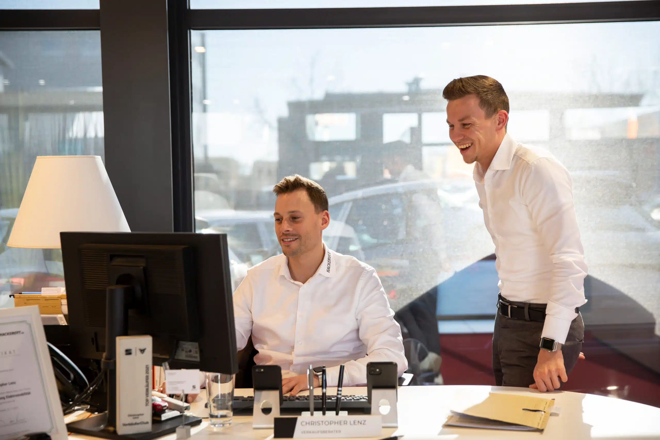 Zwei lächelnde Hackerott-Mitarbeiter betrachten gemeinsam einen Computerbildschirm im Büro.