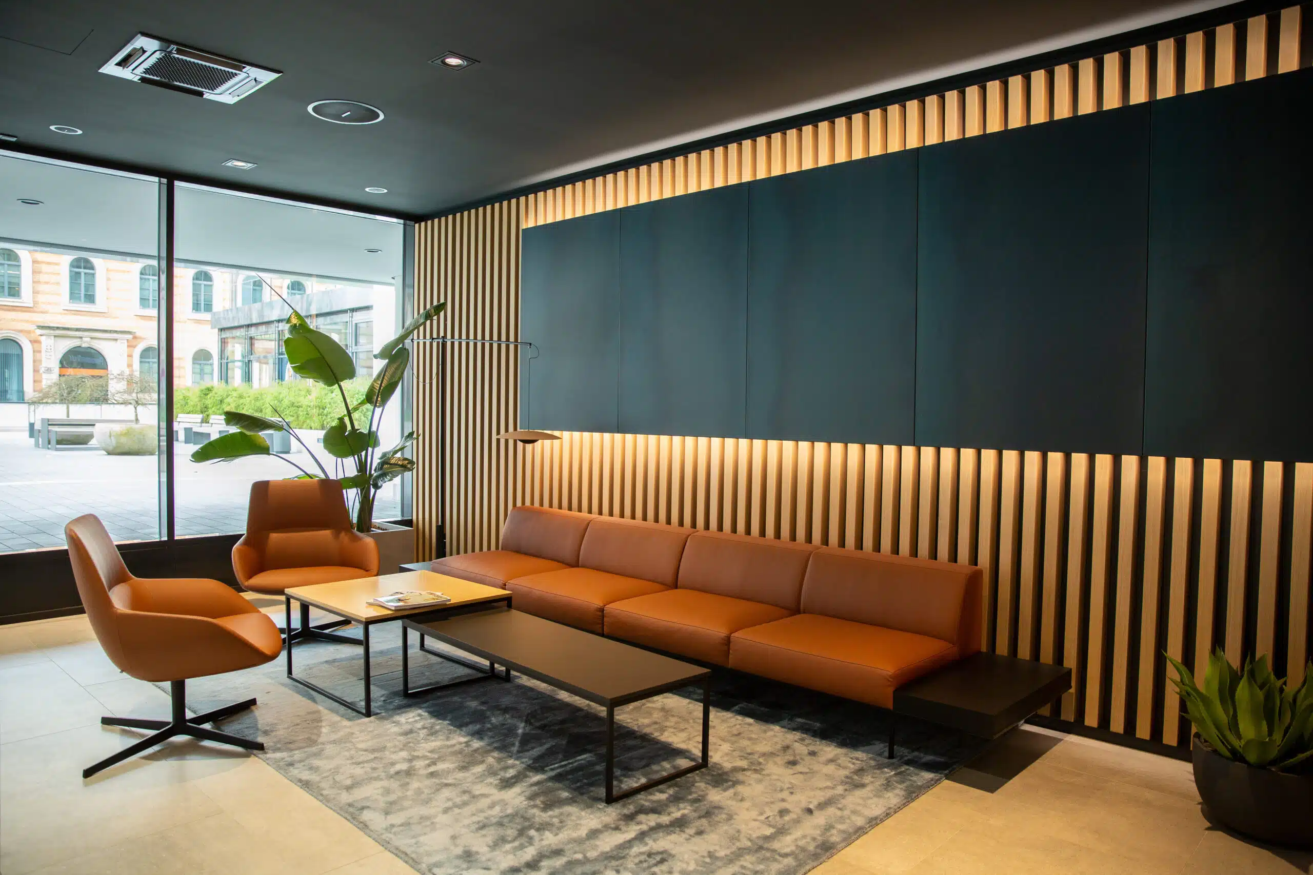 Moderner Loungebereich mit brauner Ledersitzgruppe und beleuchteter Holzlamellenwand.