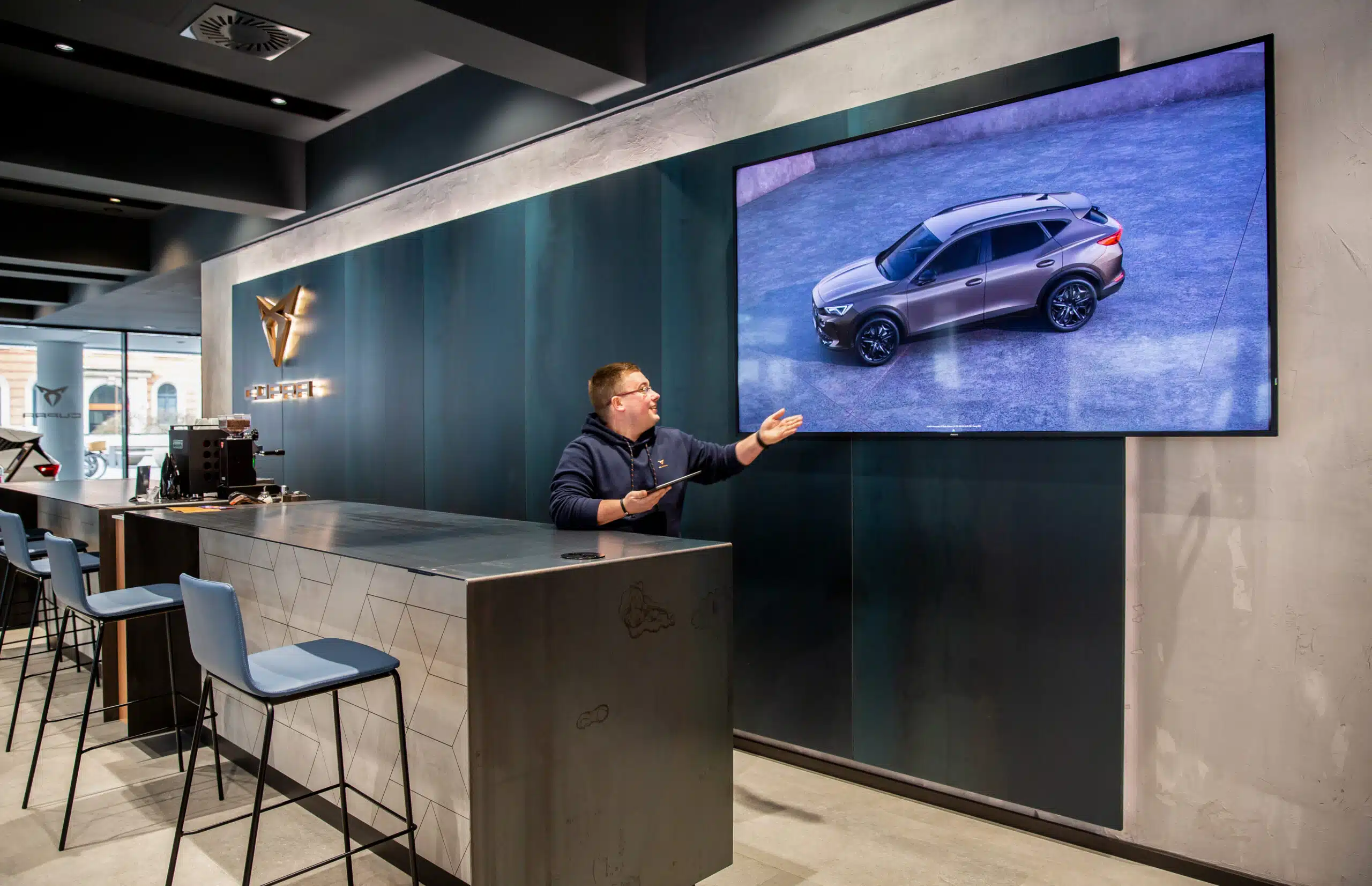 Mitarbeiter im Cupra Showroom präsentiert ein SUV-Modell auf einem Bildschirm.