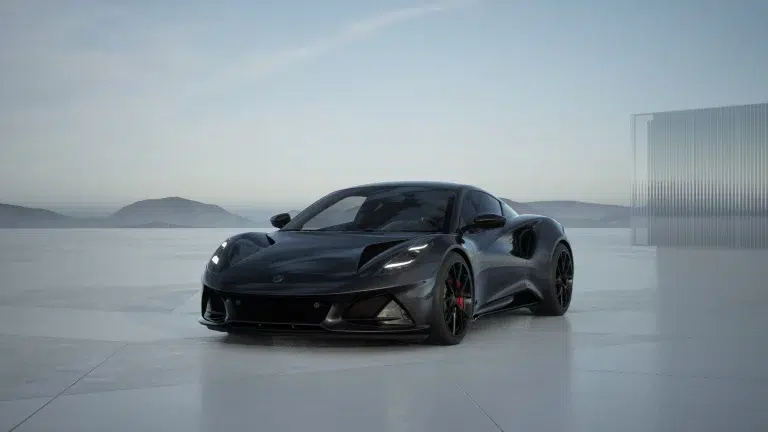 Lotus Emira Turbo SE in Cosmos Schwarz auf einer modernen Fläche vor Bergen, Wasser und einer Glaswand.