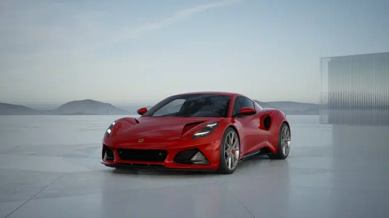 Der leuchtend rote Lotus Emira Turbo Sportwagen steht auf einer hellen Fläche vor einer bergigen Landschaft und einer modernen Glaswand.