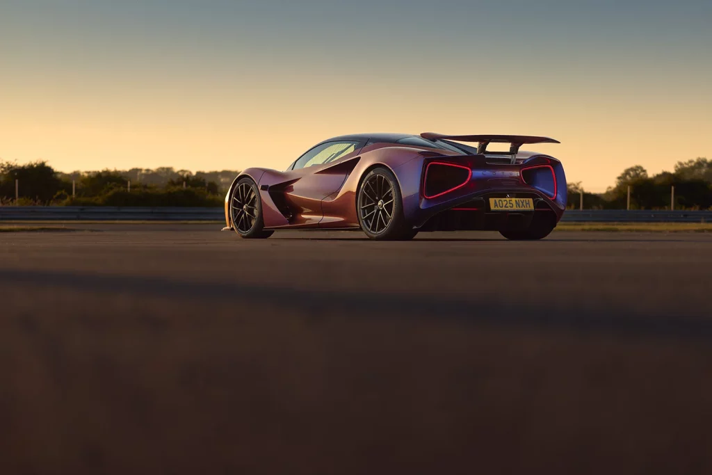 Heckansicht des Lotus Evija in schillernder Lackierung mit markanten roten Rückleuchten auf einer Rennstrecke bei Sonnenuntergang.