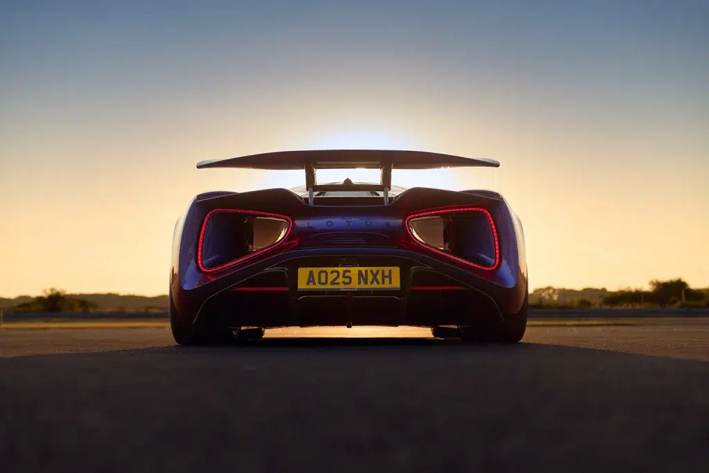 Dunkelblaue Heckansicht des Lotus Evija mit leuchtenden roten Rückleuchten und großem Heckflügel bei Sonnenuntergang.