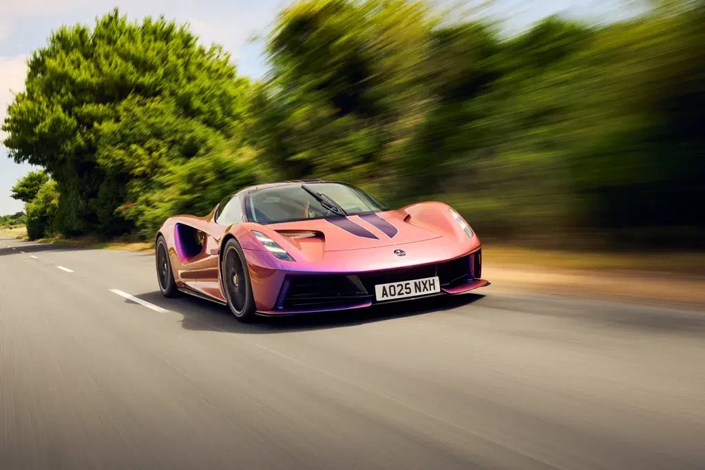 Der schillernde Lotus Evija Hypercar in Pink und Lila fährt dynamisch auf einer Landstraße.