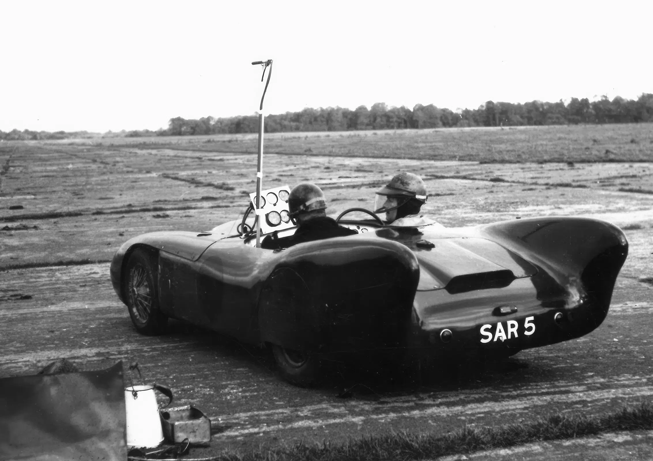 Klassischer Lotus Rennwagen SAR 5 mit zwei Helmfahrern und Messinstrumenten auf einem Flugfeld.