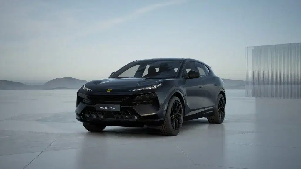 Ein dunkelgrauer Lotus Eletre Elektro-SUV steht auf einem modernen Vorplatz vor Bergen und einer Glaswand.